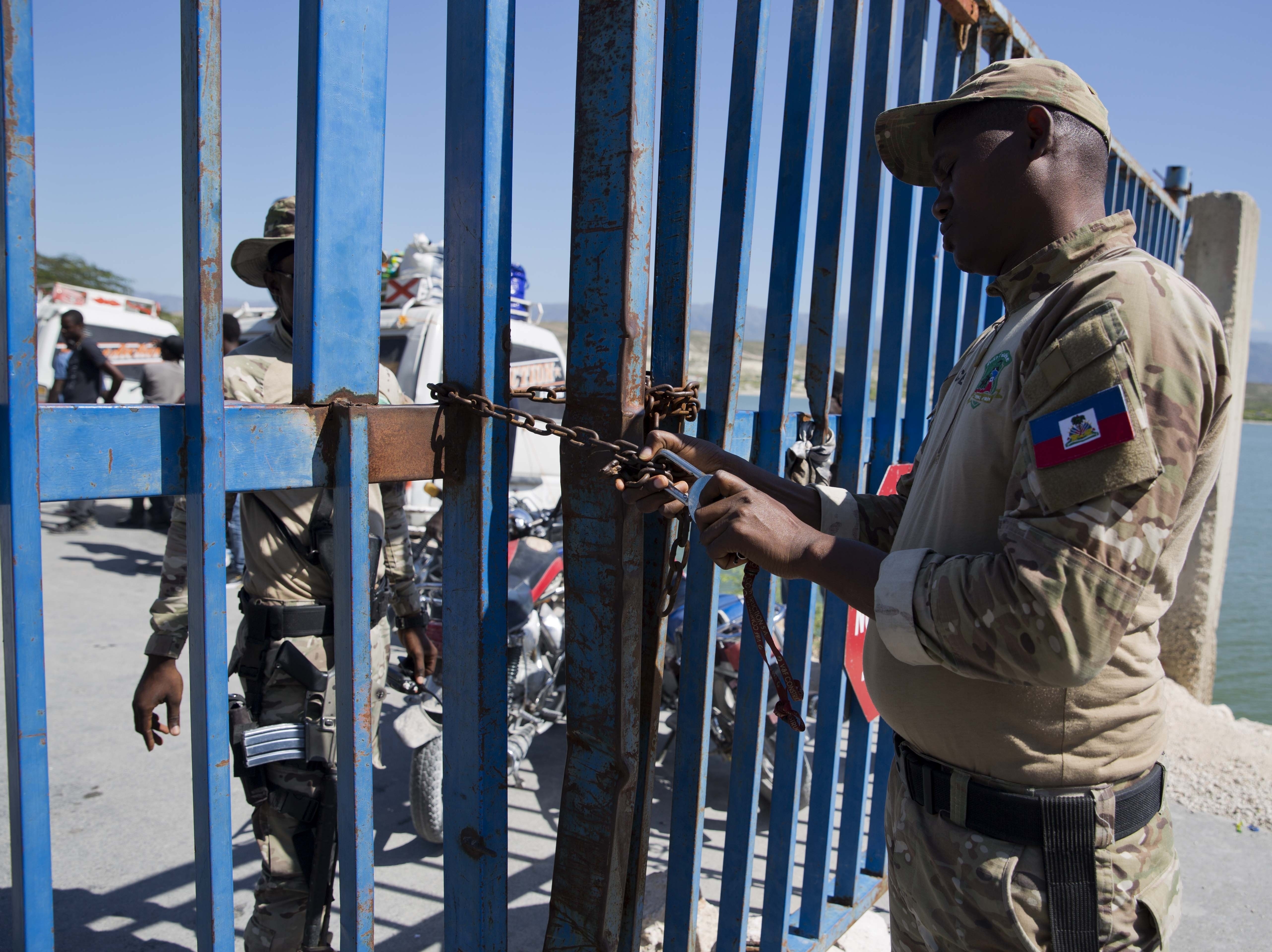 caption: A Haitian police officer locks a gate that separates the Dominican Republic border town Jimani from Malpasse, Haiti, last month, as Haitian authorities shut down the border because of concerns over the spread of COVID-19.