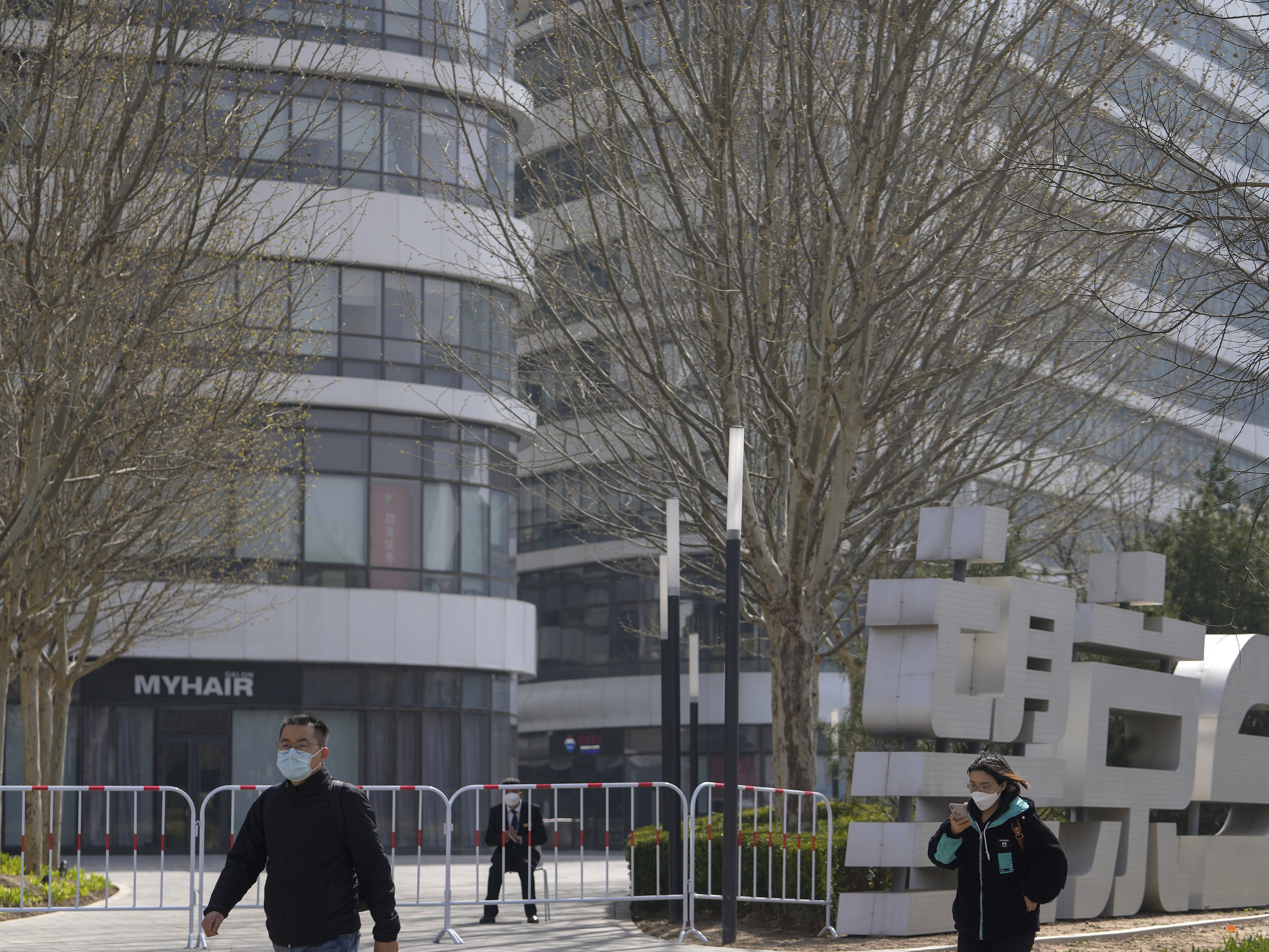 caption: Residents wearing face masks walk by a masked security watch over a barricaded Galaxy Soho commercial office building locked down for health monitoring following a COVID-19 case detected in the area Tuesday in Beijing. China has sent more than 10,000 health workers from across the country to Shanghai, including 2,000 military medical staff.