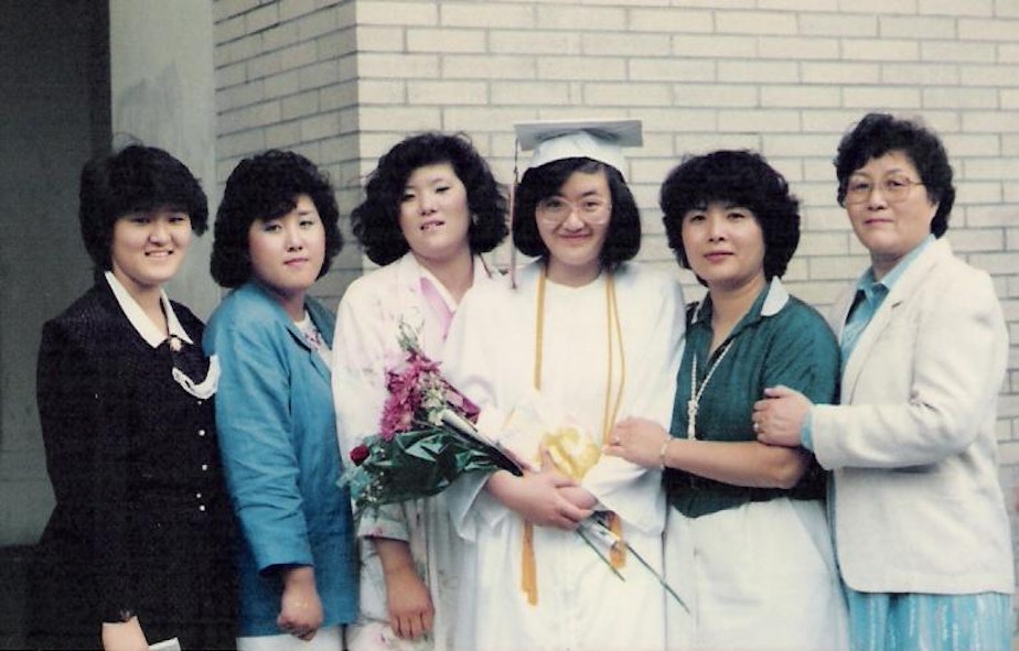 caption: Sue Lim with her mom and four of her sisters (from left: Andria Sueyoung Kim, Jackie Hyekoung Ro, Hyeyoung Lim, Sue Lim, Nancy Junghee Lee, and Eui Bun Lim) at her graduation from Rainier Beach High School in 1986. Sue immigrated to the U.S. at age 16. 