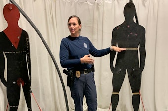 caption: Sgt. Theresa Magyera, who oversees training and recruitment, stands near figures used to teach less lethal weapons methods.