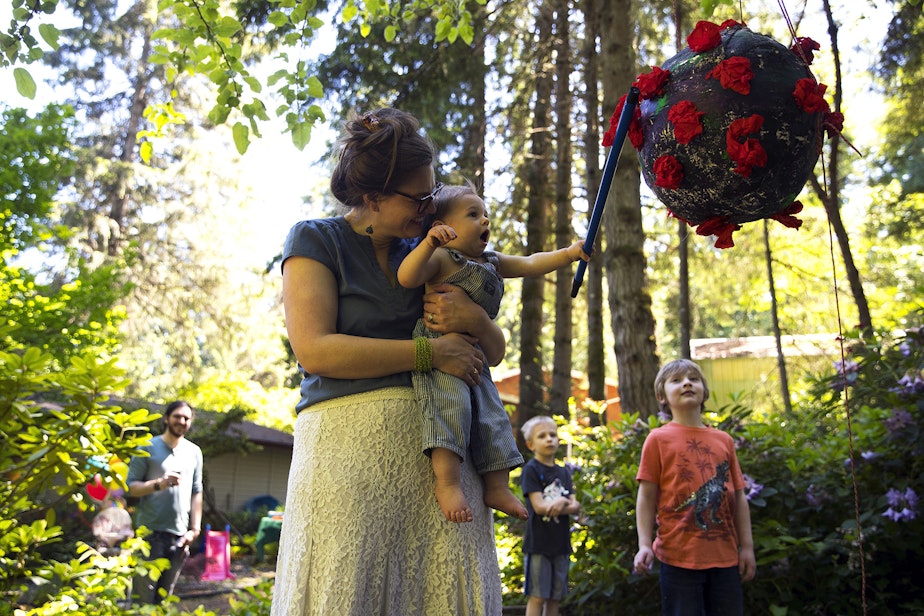 caption: Hope Black holds her son, Arlo, as he hits a homemade coronavirus themed piñata during his 1st birthday party on Saturday, May 29, 2021, in the backyard of their home on Vashon Island.