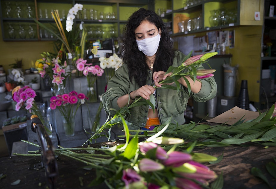 caption: Dory, an employee at Pike Place Flowers, removes leaves while making a bouquet on Friday, October 2, 2020, in Seattle.