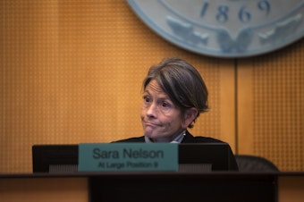 caption: Seattle City Council President Sara Nelson reacts during the public comment period of a city council meeting on Tuesday, February 27, 2024, at Seattle City Hall. Asylum seekers once housed at the Sleep Inn in SeaTac, marched to Seattle City Hall along with activists, mutual aid organizations and allies to ask for assistance with housing.   