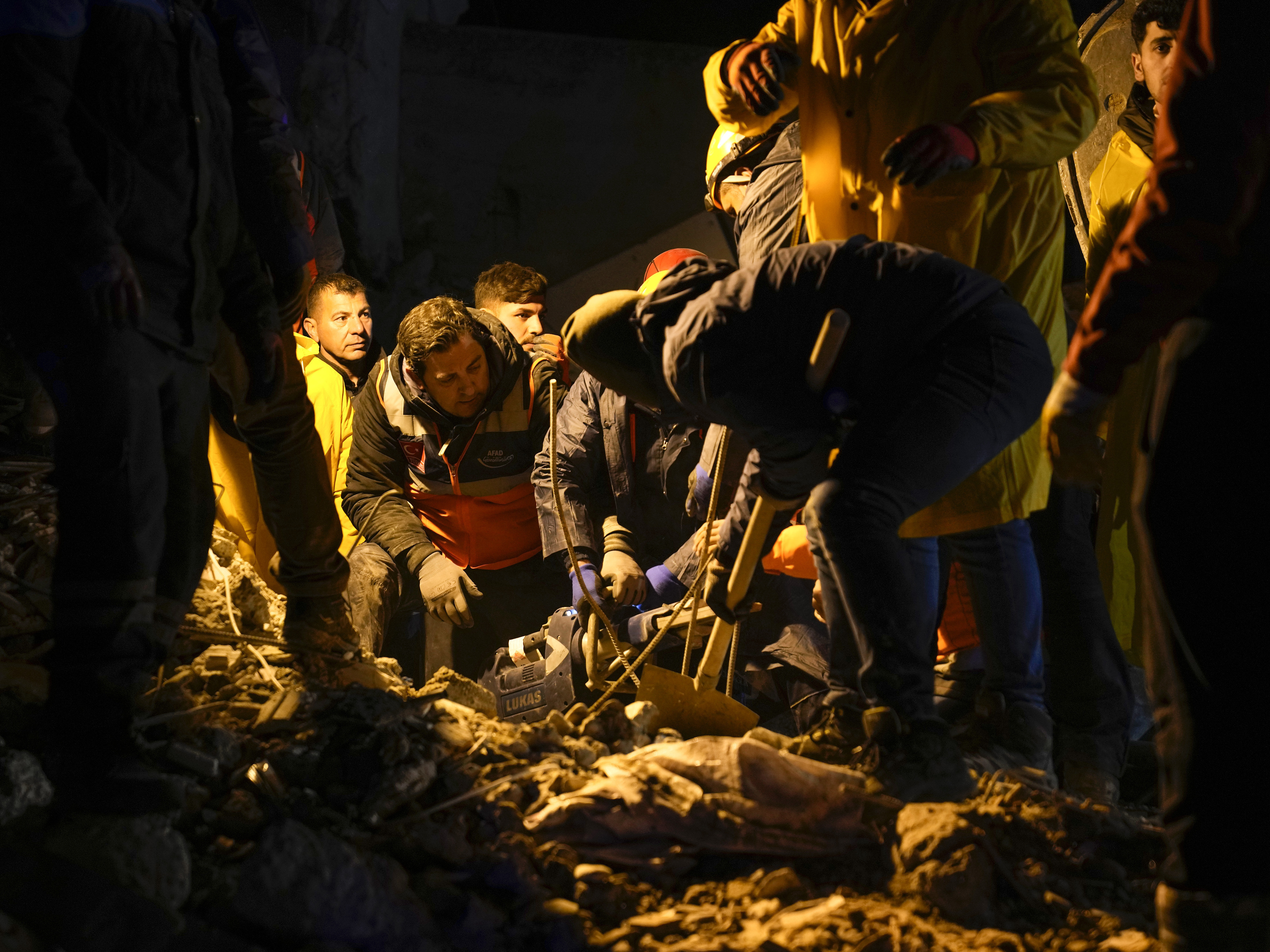 caption: Emergency teams search in the rubble for people in a destroyed building in Adana, Turkey, on Monday.