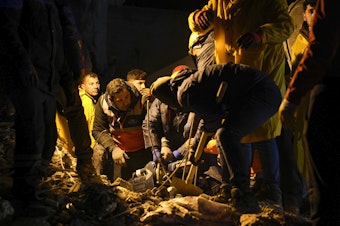 caption: Emergency teams search in the rubble for people in a destroyed building in Adana, Turkey, on Monday.