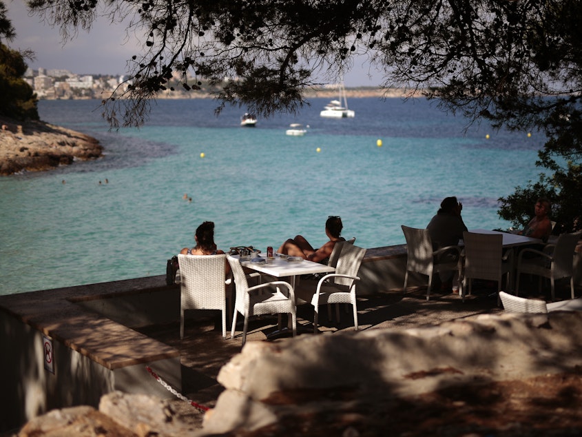 caption: The European Union has decided on its first list of approved travel partners, as part of its reopening of external borders. Here, people sit in a terrace bar at the beach in Palma de Mallorca, Spain, earlier this month, when many internal travel restrictions were lifted.