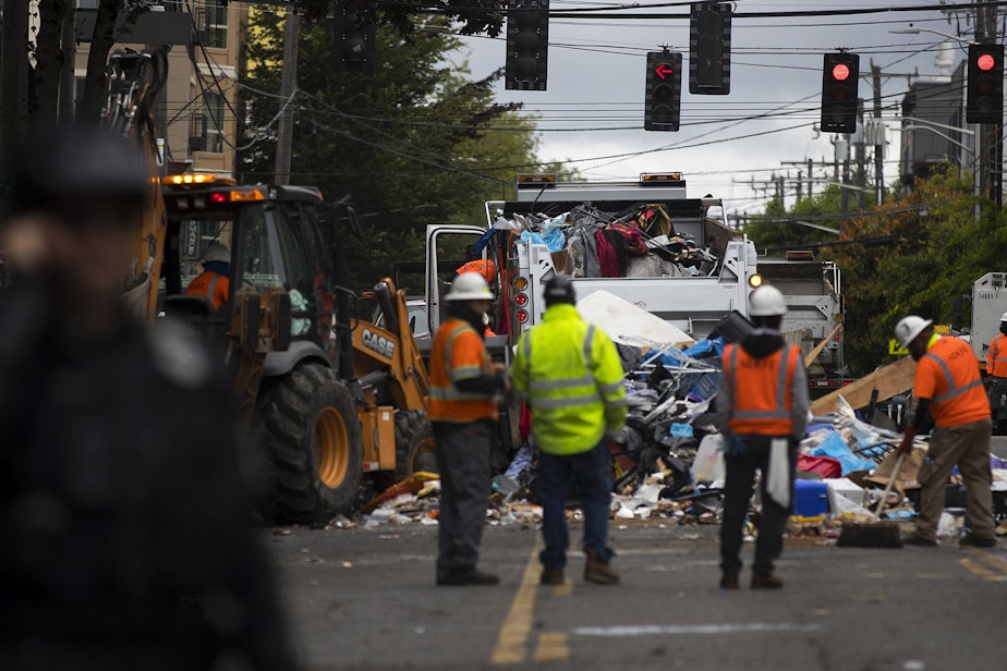 caption: Seattle Department of Transportation employees use bulldozers to remove items from outside of the East Precinct building and place them into dumpsters after the Capitol Hill Organized Protest zone was cleared by Seattle Police Department officers early Wednesday morning, July 1, 2020, in Seattle.