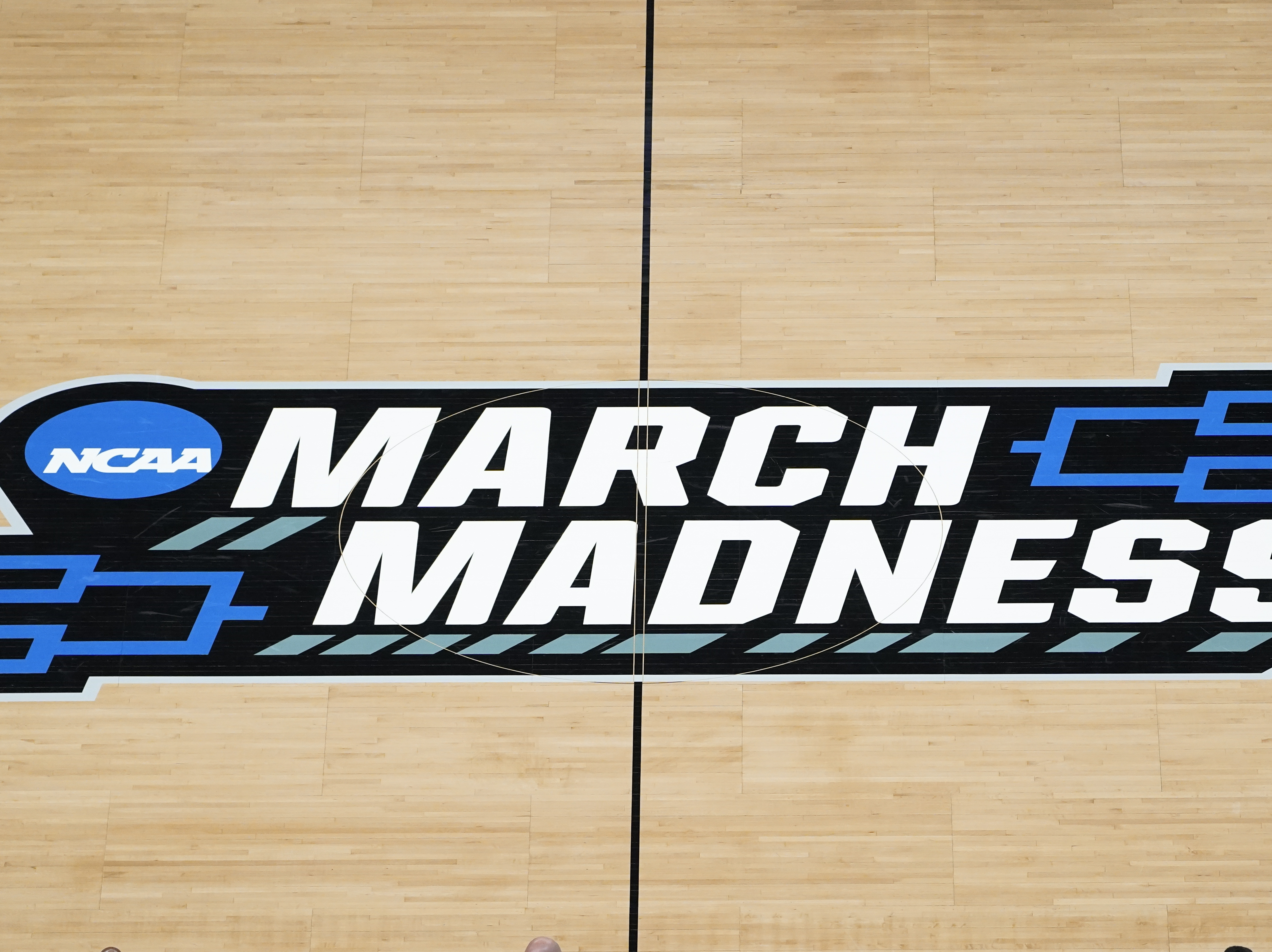 caption: The March Madness logo is shown on the court during the first half of a men's college basketball game in the first round of the NCAA tournament at Bankers Life Fieldhouse in Indianapolis. The Supreme Court eroded<strong> </strong>the difference between elite college athletes and professional sports stars.