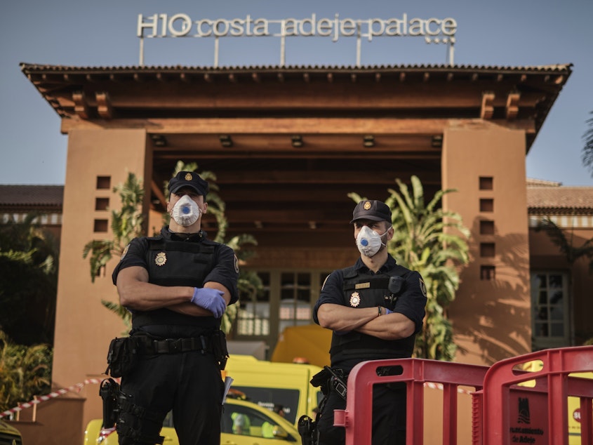 caption: The virus that causes COVID-19 is now found in 37 countries outside of China, WHO Director-General Tedros Adhanom Ghebreyesus says. Here, police officers wear face masks in front of a hotel in the Canary Island of Tenerife, Spain, Wednesday. Spanish officials say a tourist hotel on island has been placed under quarantine after an Italian doctor staying there tested positive for the coronavirus.