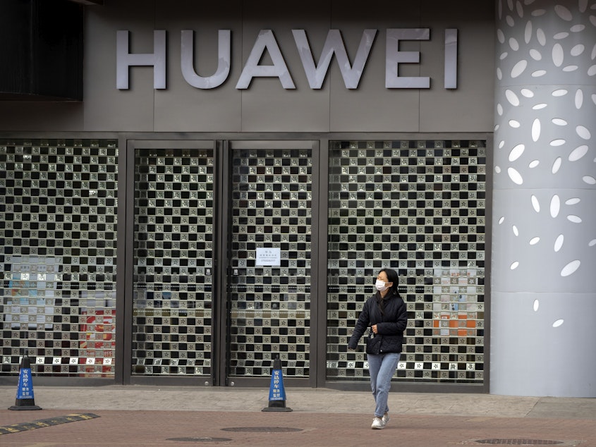 caption: A woman wearing a face mask walks past a Huawei store temporarily closed due to coronavirus-related restrictions in Beijing, Thursday, May 12, 2022. China's leaders are struggling to reverse a deepening economic slump while keeping a "zero-COVID" strategy that has shut down Shanghai and other cities.