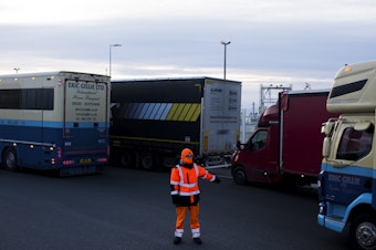 caption: A worker directs trucks where to wait in line in order to board ferries to the United Kingdom in Calais, France. Twenty percent of British imports pass through the port of Calais.