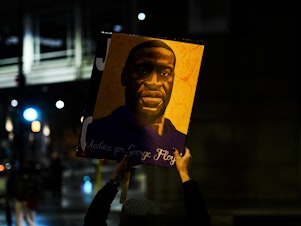 caption: A person holds up a portrait of George Floyd as people gather outside the Hennepin County Government Center on April 9 in Minneapolis