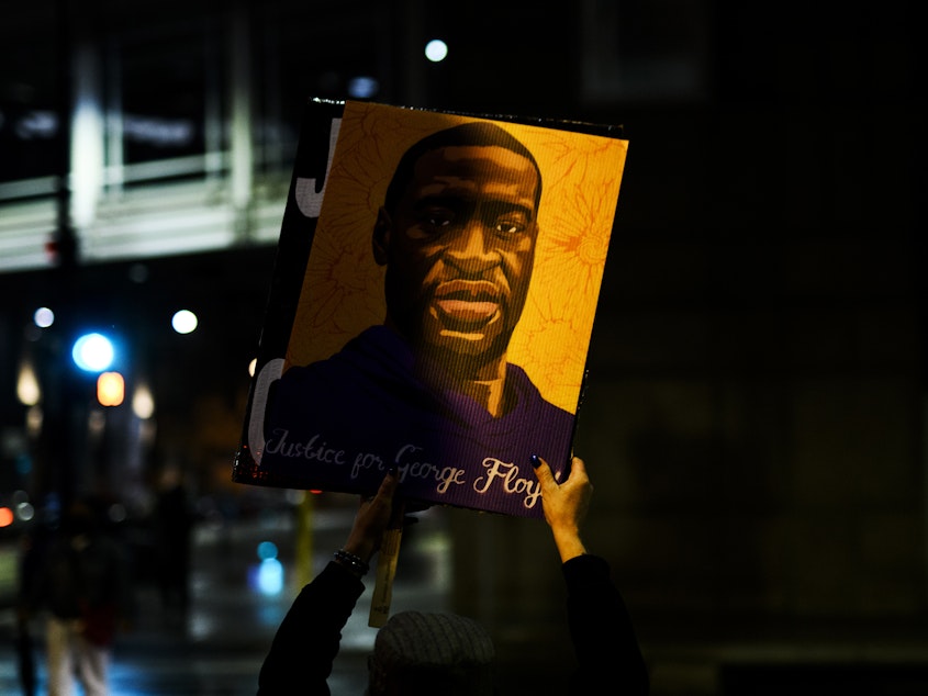 caption: A person holds up a portrait of George Floyd as people gather outside the Hennepin County Government Center on April 9 in Minneapolis