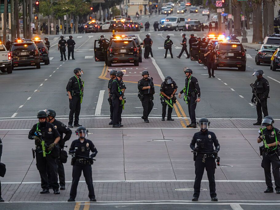 caption: Police fill the streets when the 8:00 PM curfew commences as protests continue in an approximately one-square mile area of downtown Los Angeles in response to a series of immigration raids on June 12, 2025 in Los Angeles, California.