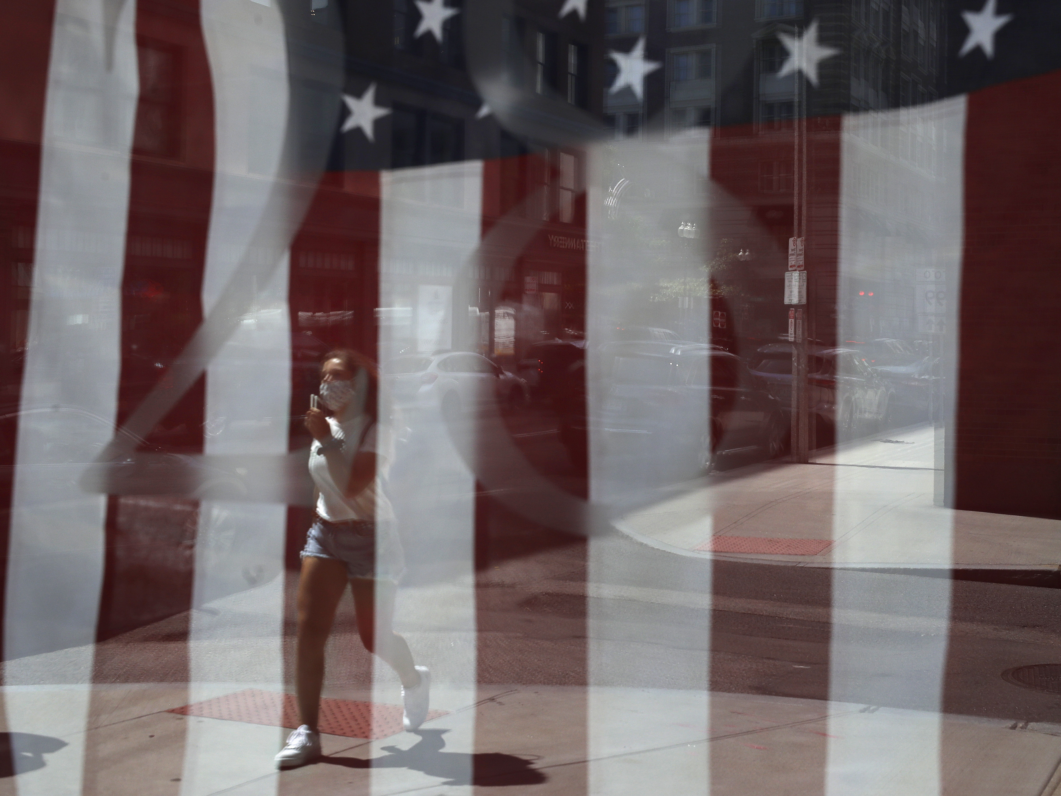 caption: A passerby wears a mask out of concern for the coronavirus while walking past an American flag displayed in Boston on Tuesday. The U.S. has now recorded more than 3 million confirmed cases of the coronavirus.