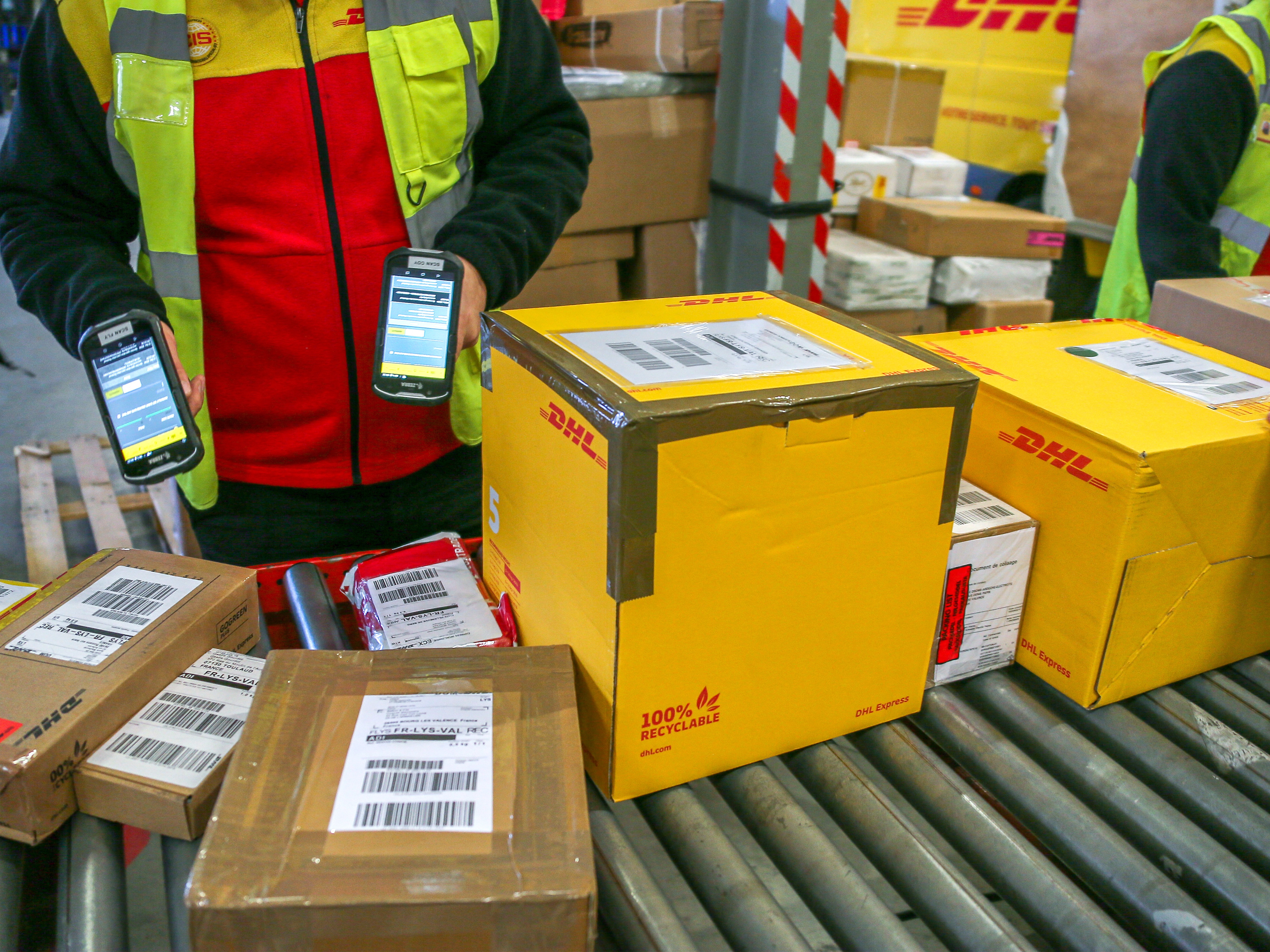 caption: A warehouse worker uses a scanner to identify cartons of parcels of goods on a conveyor belt in a hangar at DHL's parcel distribution and express freight warehouse in Valence, France, on December 12, 2024.