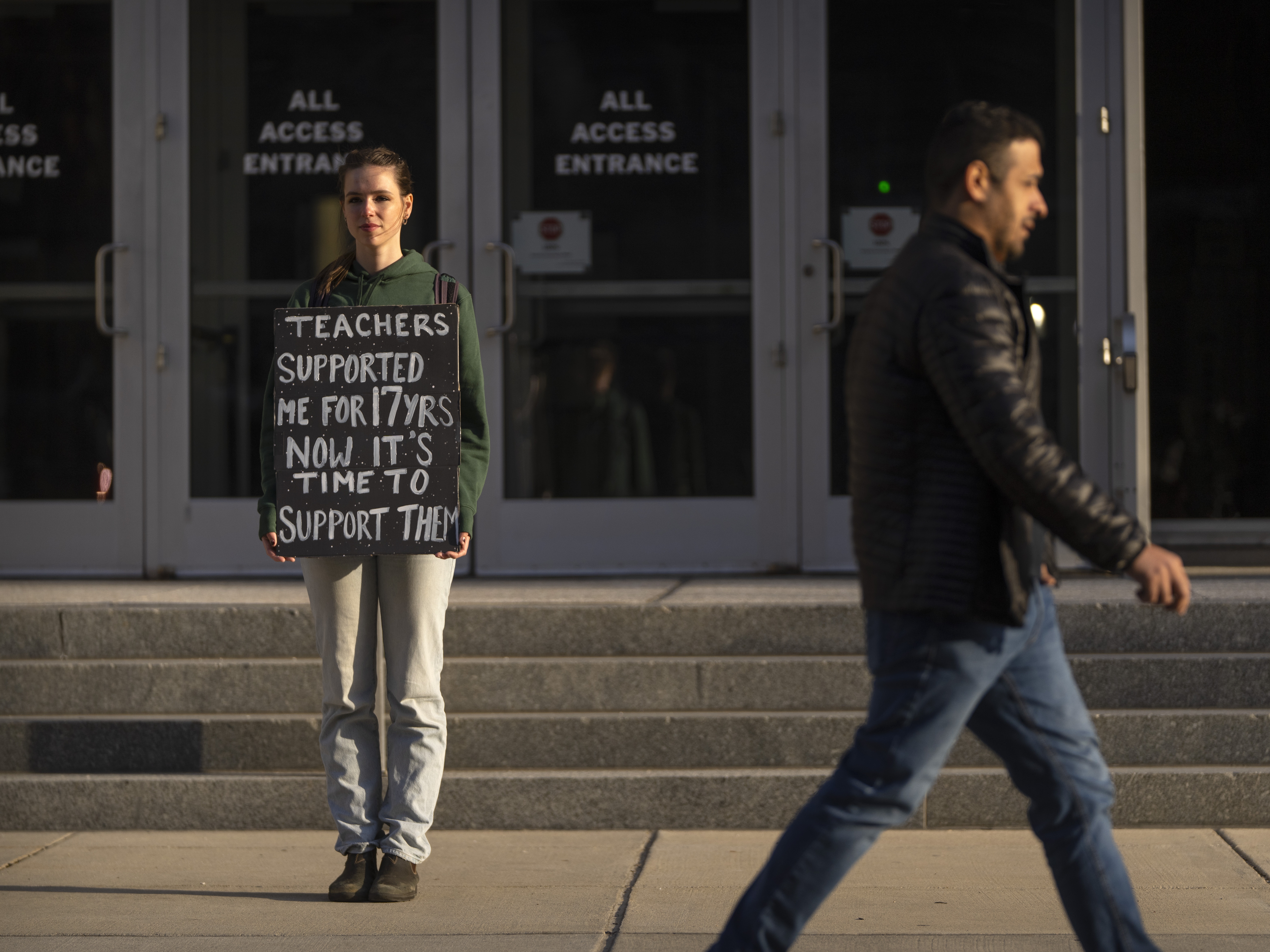 caption: Chloe Kienzle of Arlington, Va., holds a sign as she stands outside the U.S. Department of Education, in Washington, D.C., on Wednesday – the day after the Trump administration announced widespread job cuts at the agency.