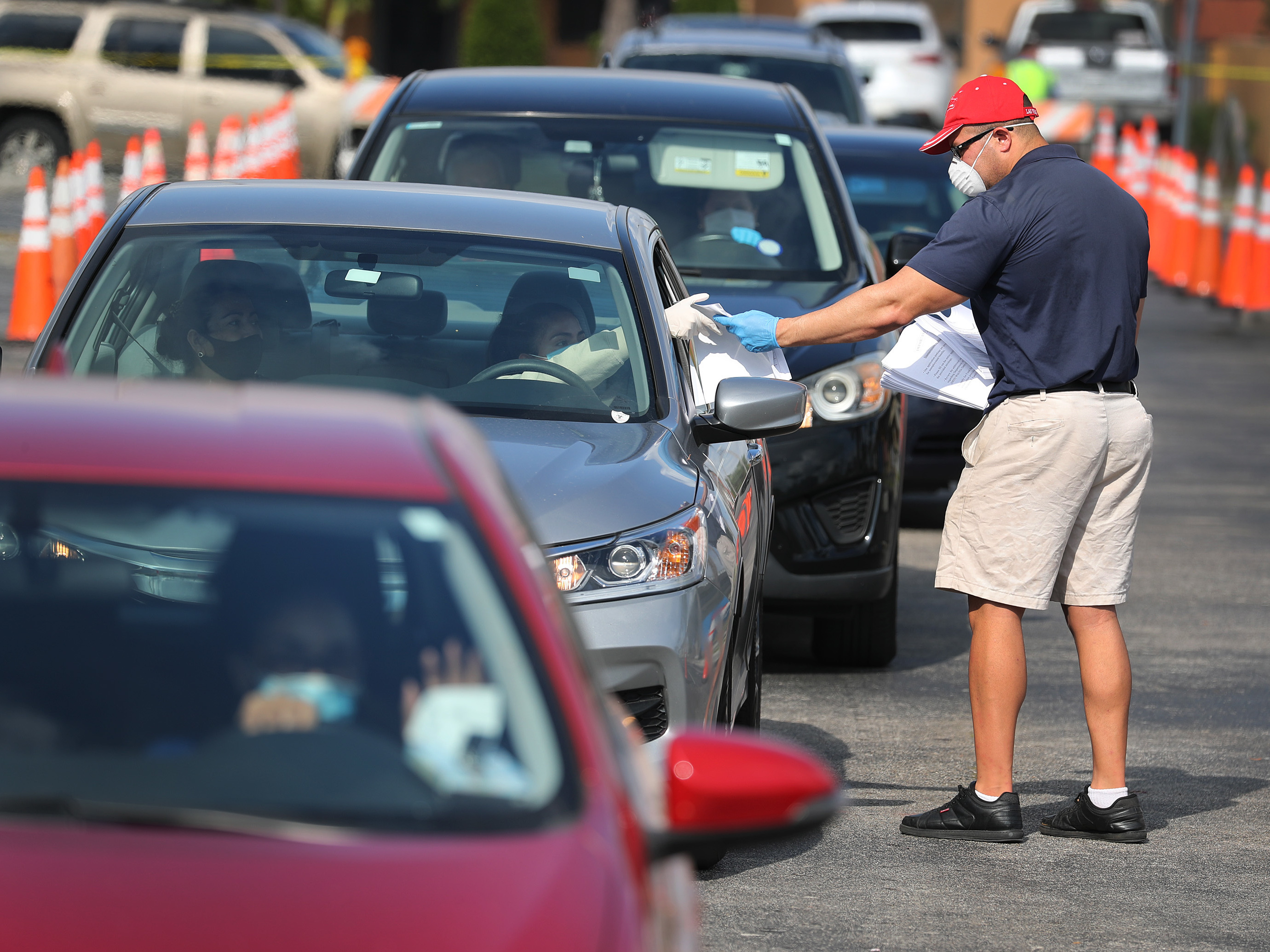 caption: Miguel Diaz, who works for the City of Hialeah, hands out unemployment applications to people in their vehicles on April 8, 2020 in Hialeah, Florida.