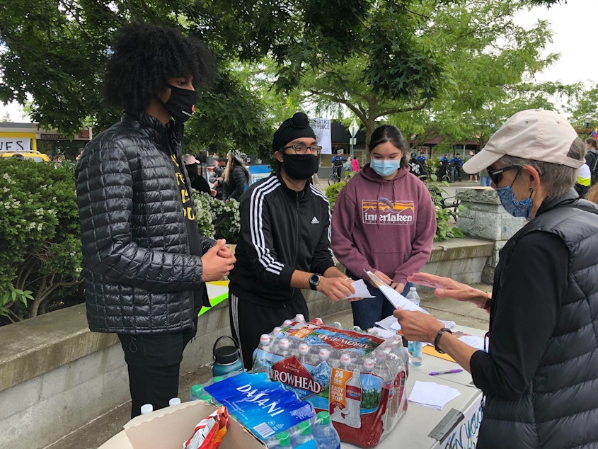 caption: Members of the Burien Youth Council take donations for protesters outside Burien City Hall.