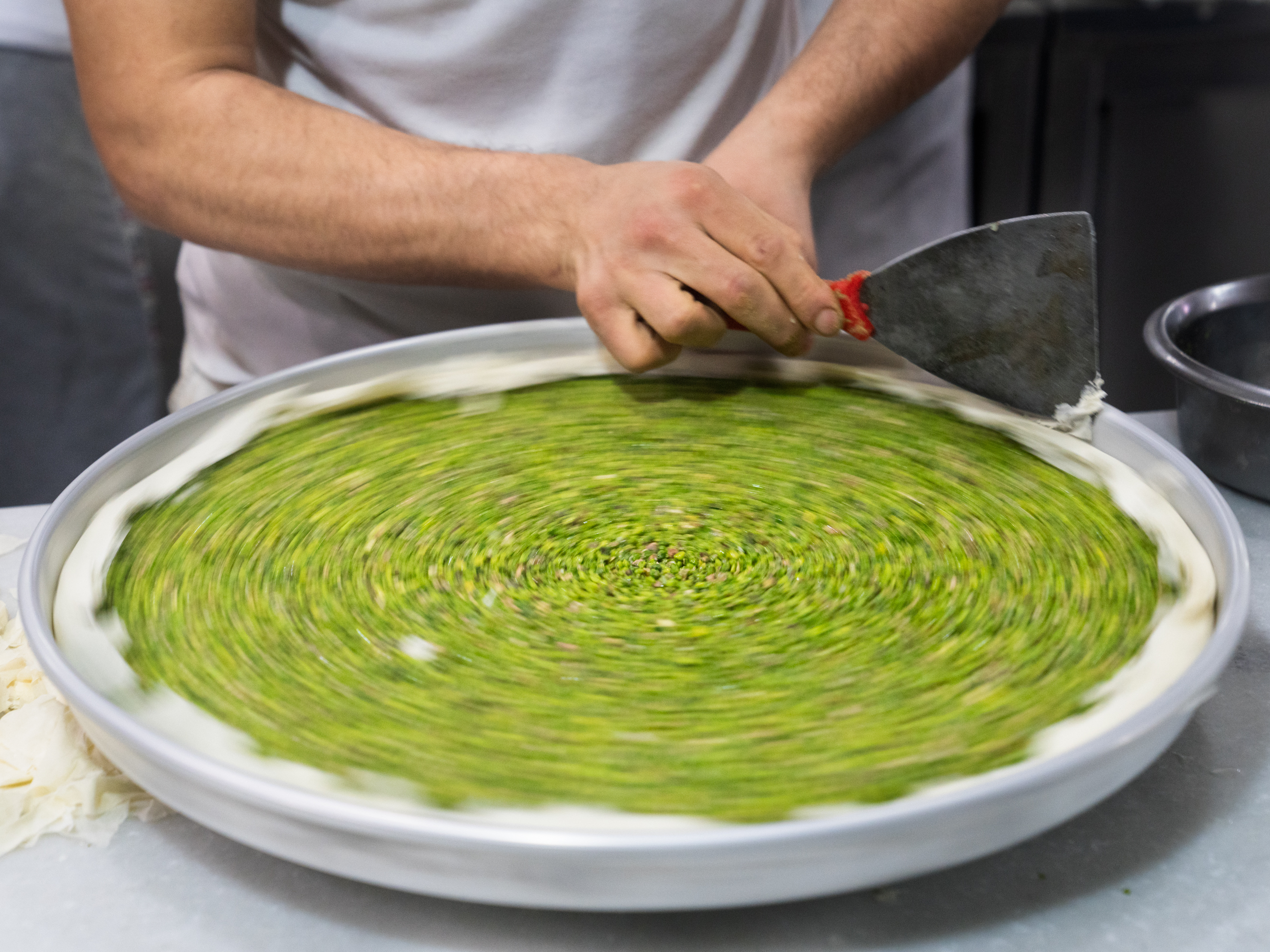 caption: A baker fine-tunes the edges of a pan of baklava before it is covered with pastry.