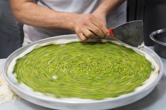 caption: A baker fine-tunes the edges of a pan of baklava before it is covered with pastry.