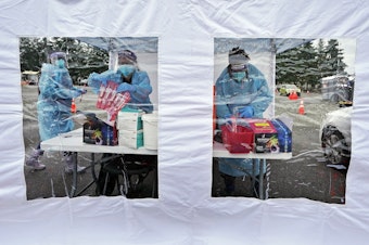 caption: FILE - Workers at a drive-up Covid-19 testing clinic stand in a tent as they prepare PCR coronavirus tests, Jan. 4, 2022, in Puyallup, Wash., south of Seattle.