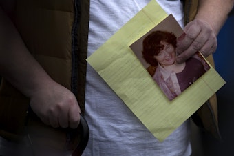 caption: Mike Weatherill holds a picture of his deceased mother, Louise Weatherill, during a press conference held by family members of residents at Life Care Center of Kirkland, outside of the facility on Thursday, March 5, 2020, in Kirkland. 