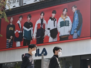 caption: People walk past a poster showing members of the K-pop group BTS in Seoul on October 12, 2020. It's one of the most popular bands in the world, with an extremely devoted fan base.