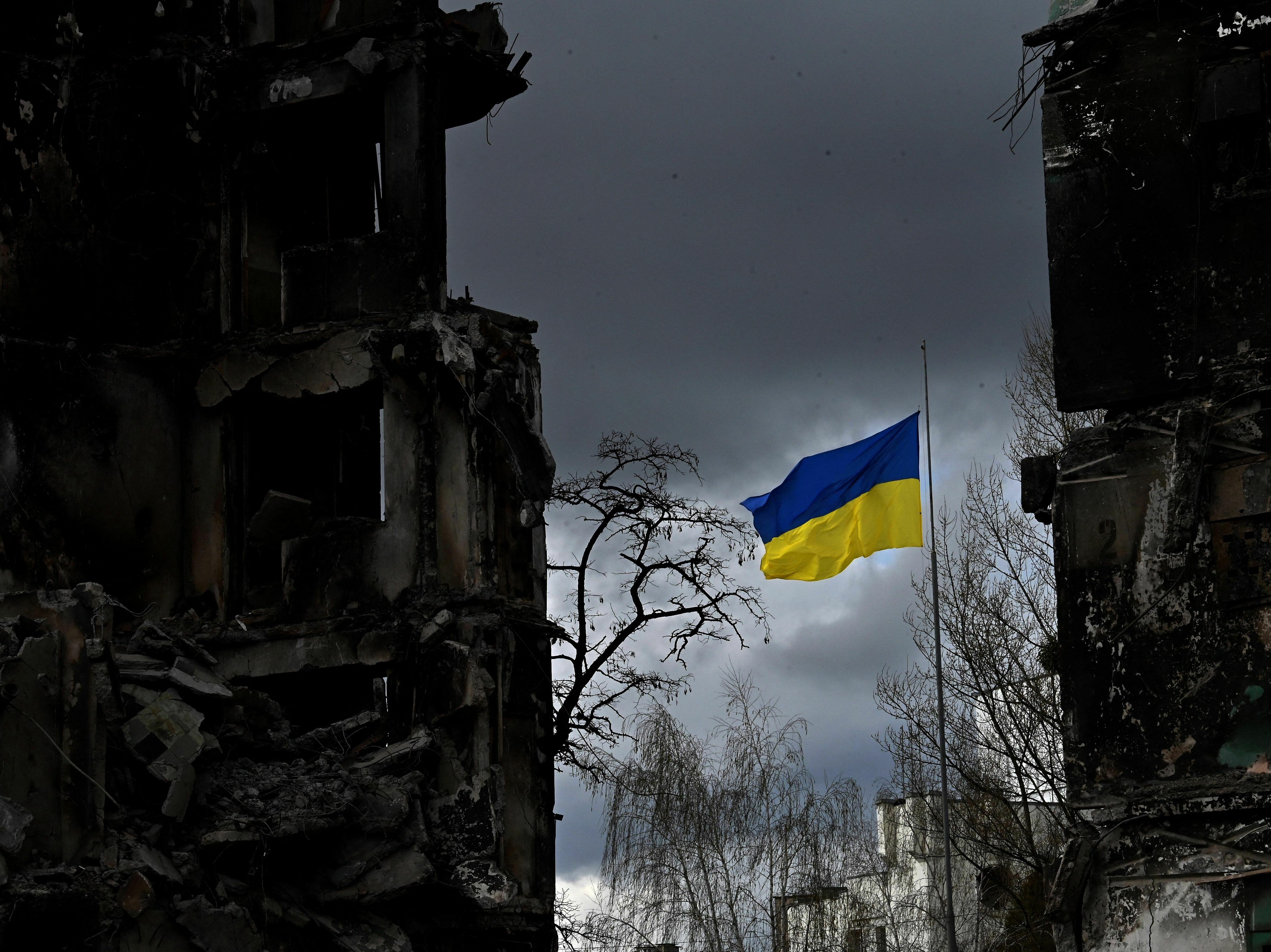 caption: The Ukrainian flag flutters between buildings destroyed in bombardment in the Ukrainian town of Borodianka. It was one year ago last week that Russia invaded.