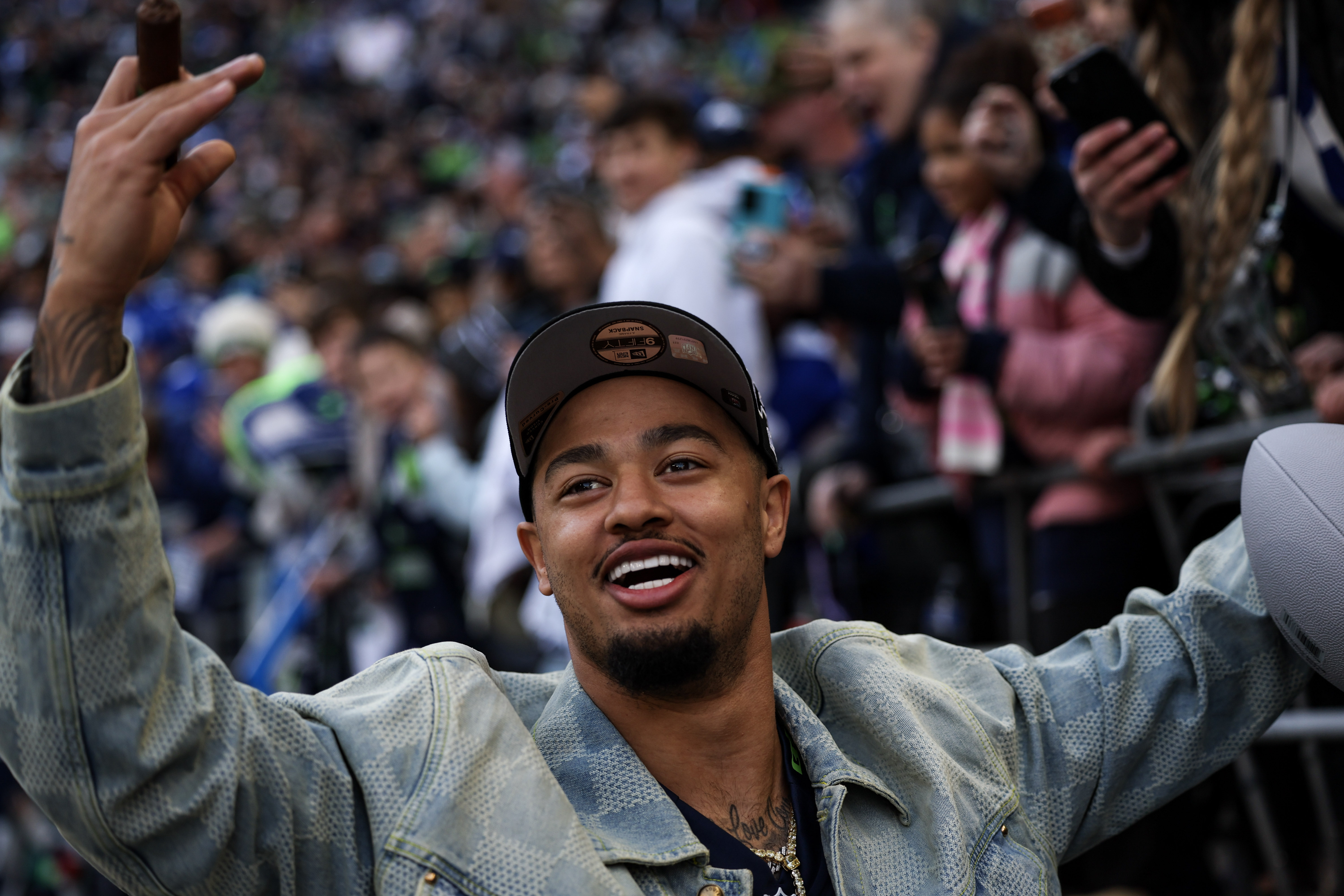 caption: Seattle Seahawks wide receiver Jaxon Smith-Njigba holds up a celebratory cigar next to fans who gathered at Lumen Field to celebrate the team's Super Bowl LX win on Wednesday, February 11, 2026.