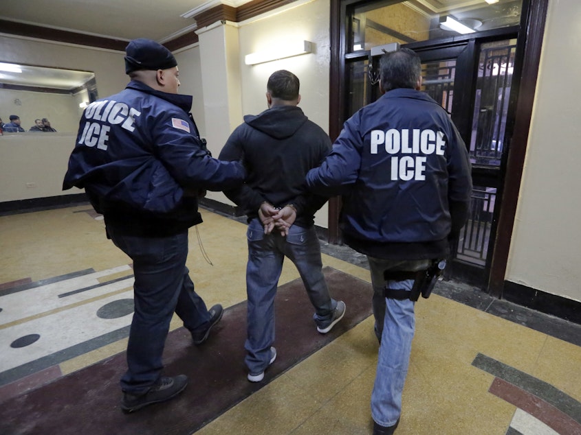 caption: In this March 3, 2015, photo, Immigration and Customs Enforcement officers escort an arrestee in an apartment building in the Bronx borough of New York during a series of early morning raids.
