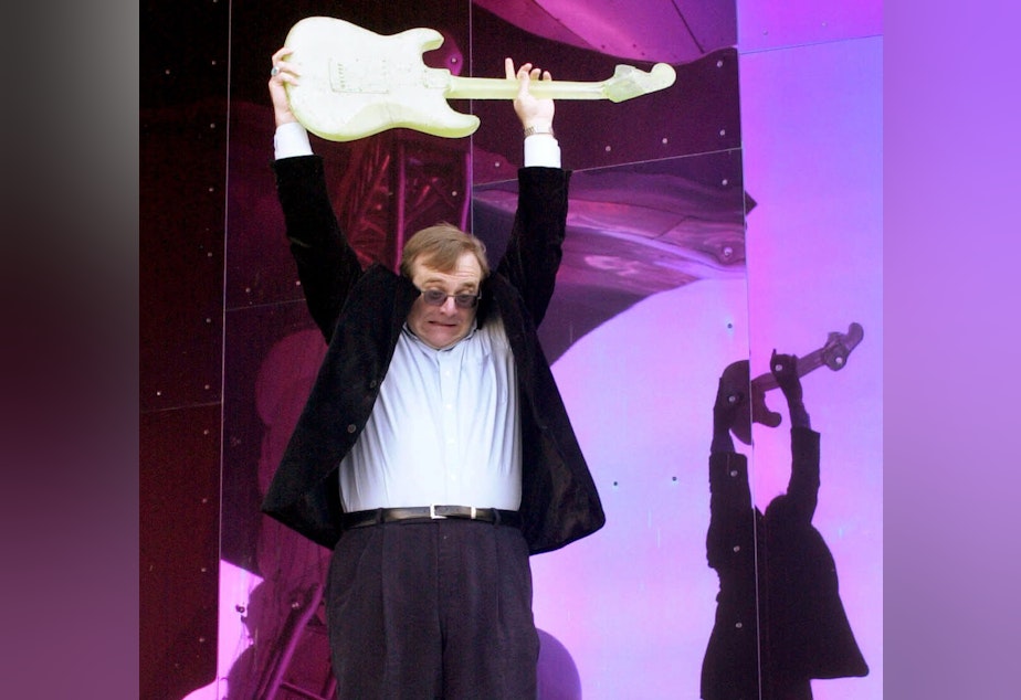 caption: Paul Allen lifts a Dale Chihuly glass guitar above his head before smashing it to open the Experience Music Project museum in Seattle on June 23, 2000.
