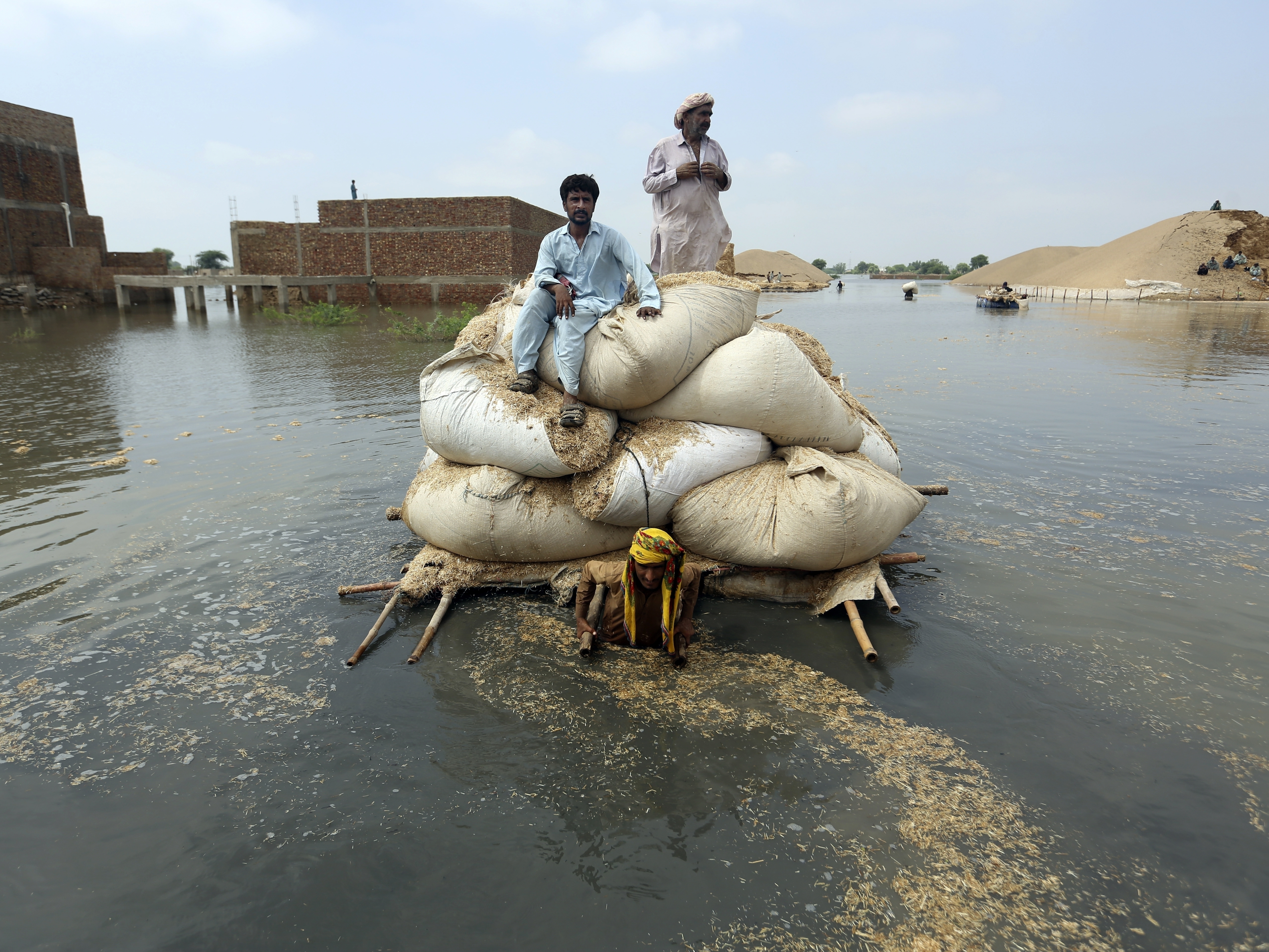 caption: Residents of southwest Pakistan move through floodwaters in September 2022. People with less wealth are more vulnerable to the effects of climate change, including more severe rainstorms.