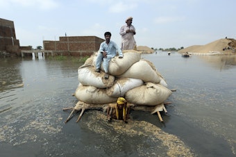caption: Residents of southwest Pakistan move through floodwaters in September 2022. People with less wealth are more vulnerable to the effects of climate change, including more severe rainstorms.