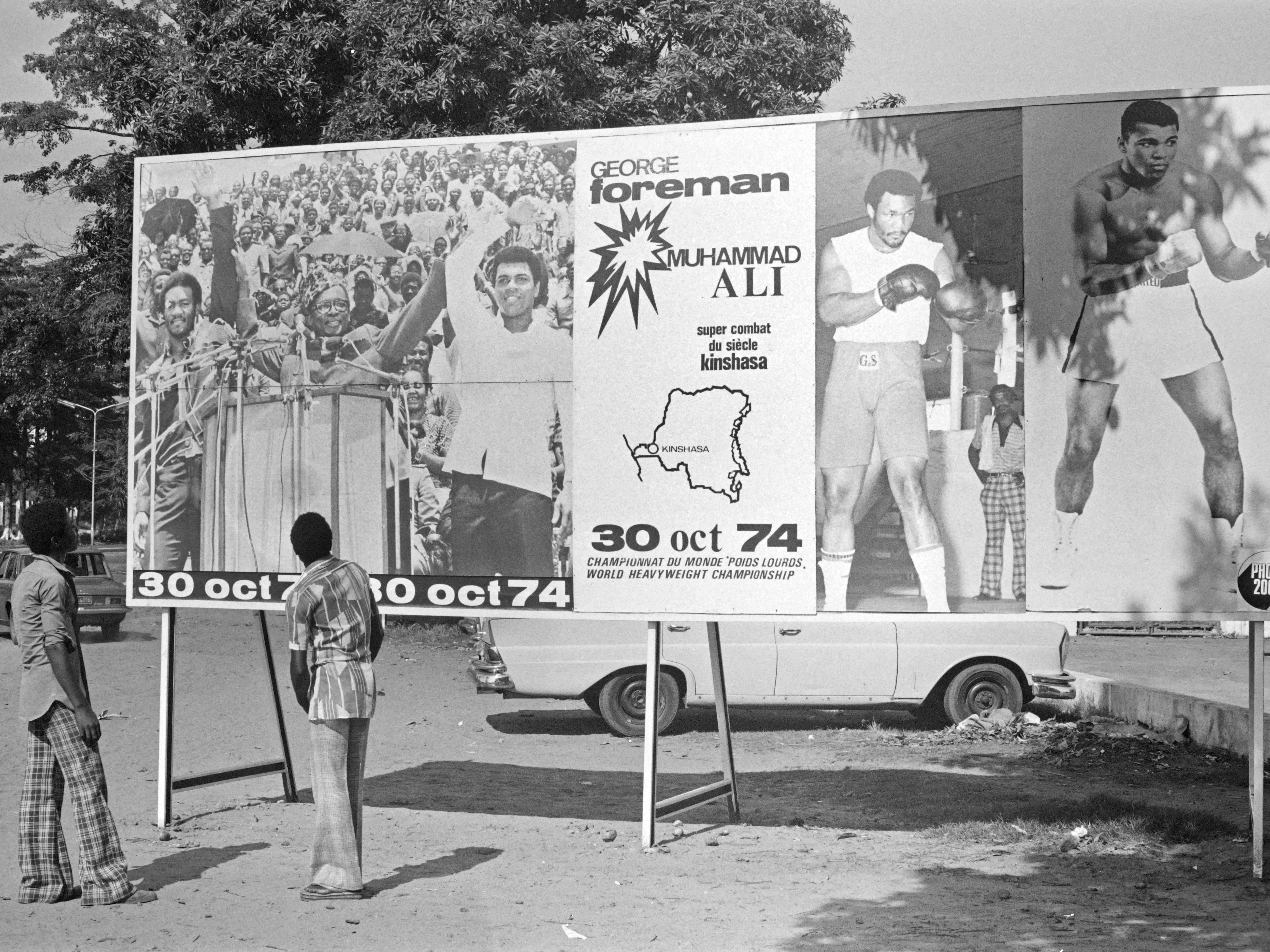 caption: People look at a billboard in Kinshasa on Oct. 30, 1974, announcing the fight between U.S. boxers Muhammad Ali and George Foreman. That day, Ali knocked out Foreman in a clash of titans known as the "Rumble in the Jungle," watched by 60,000 people in the stadium in Kinshasa and millions elsewhere.