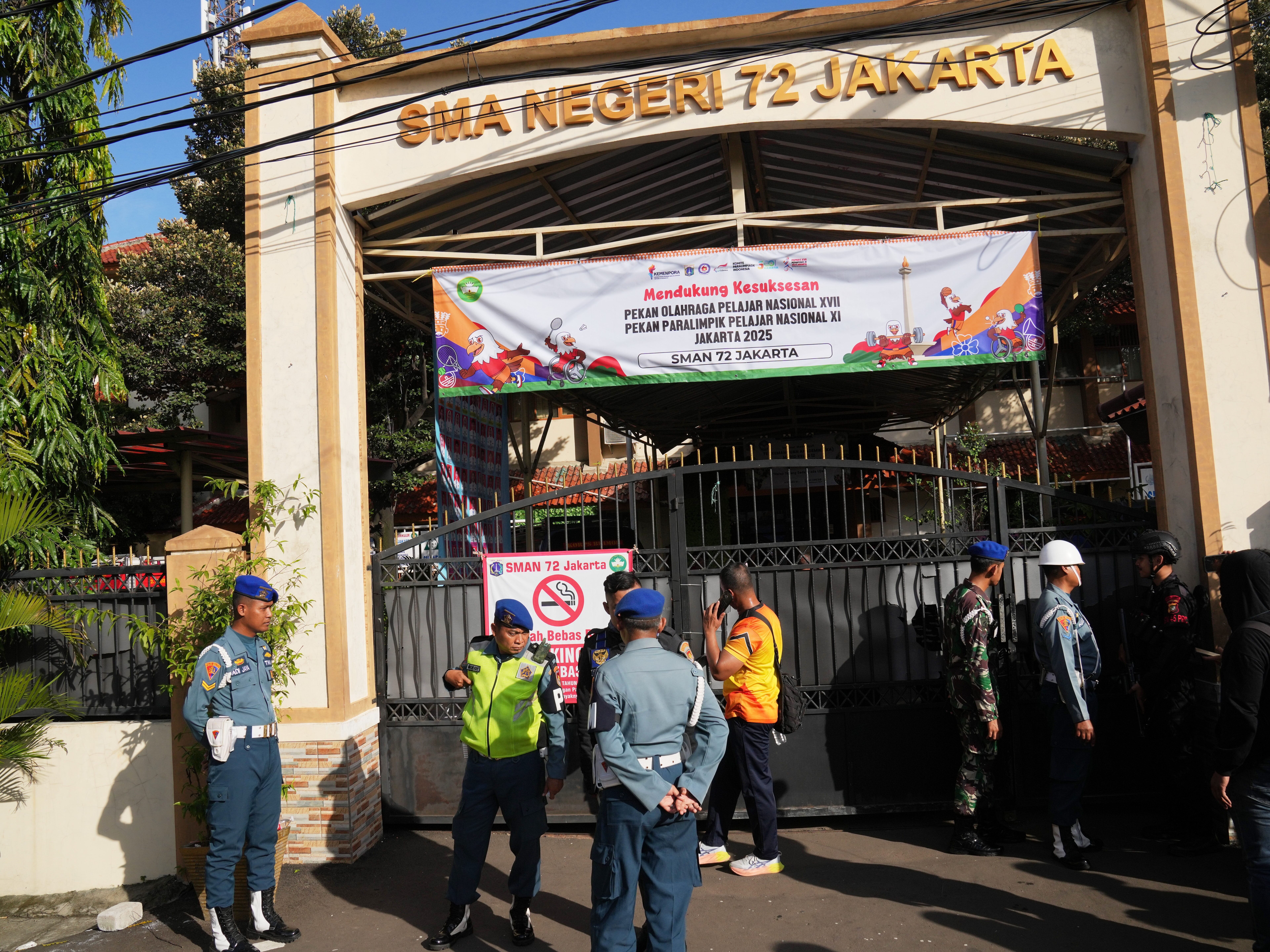 caption: Police officers and military personnel stand guard at the gate of a school where explosions reportedly occurred, in Jakarta, Indonesia, Friday.