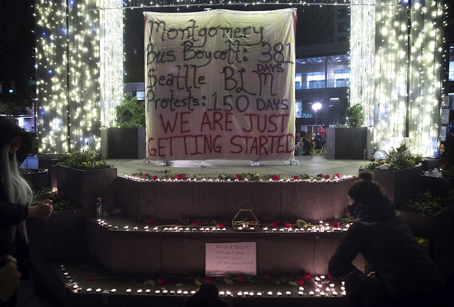 caption: Following speeches from organizers, lit candles were placed around a banner during the 150th day of protests for racial justice in Seattle on Monday, October 26, 2020, at Westlake Park. The other side of the banner reads, 'You can't stop this revolution.' 