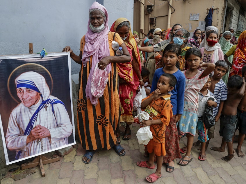 caption: Homeless people gather beside a portrait of Saint Teresa, the founder of the Missionaries of Charity, to collect free food outside the order's headquarters in Kolkata, India, in August.