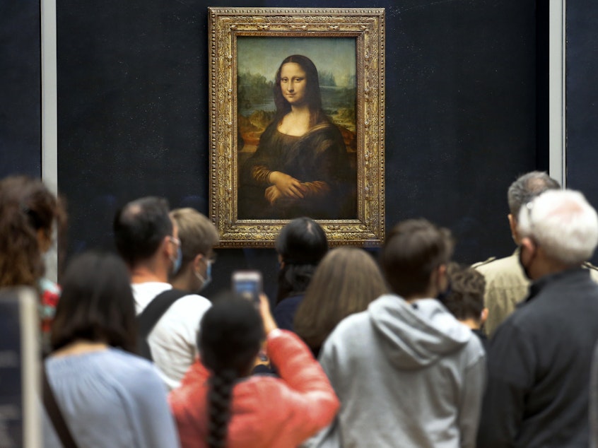 caption: Visitors wearing face masks wait to see the <em>Mona Lisa</em> at the Louvre Museum on Monday. The most visited museum in the world reopened to the public after closing in March.