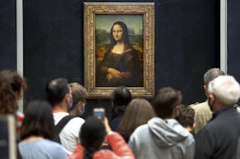 caption: Visitors wearing face masks wait to see the <em>Mona Lisa</em> at the Louvre Museum on Monday. The most visited museum in the world reopened to the public after closing in March.