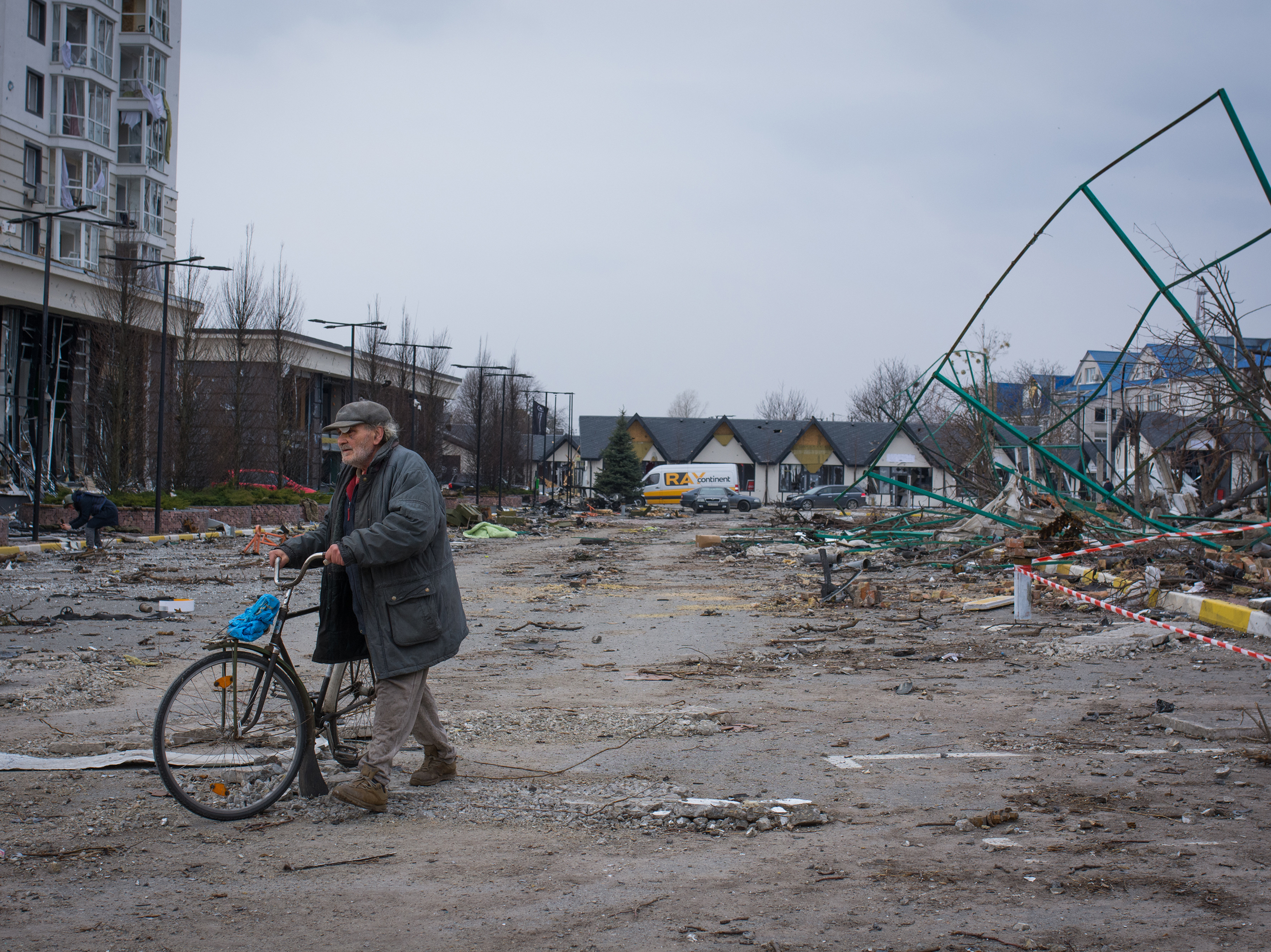 caption: A man walks his bike through a parking lot littered with broken glass in Bucha, Ukraine.