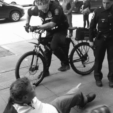 caption: Seattle police approach man on the street, part of the group show, We are still here, at Gallery4Culture.