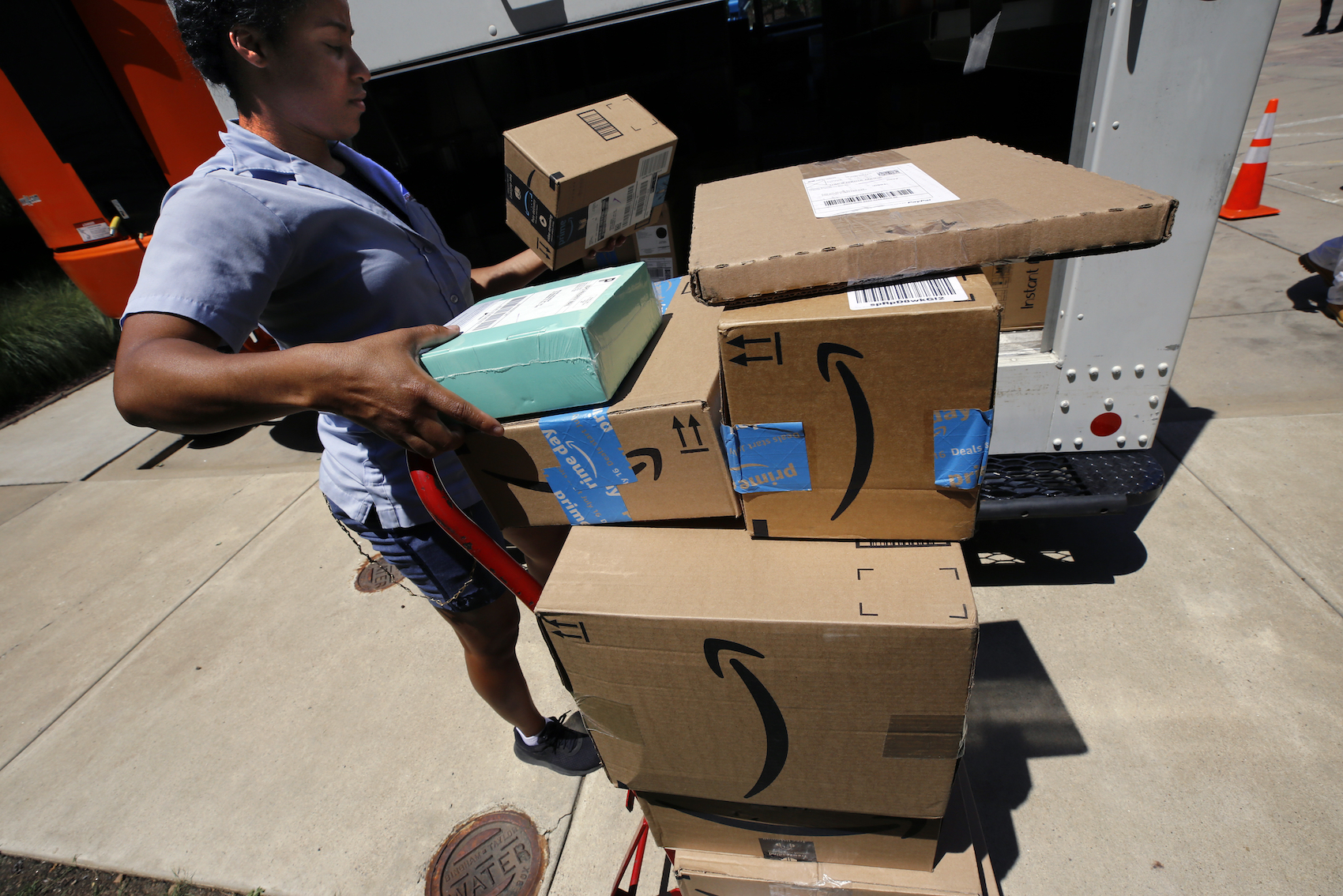caption: In this July 19, 2018, photo, a U.S. postal carrier delivers Amazon orders to an apartment complex in downtown Pittsburgh. (Gene J. Puskar/AP)