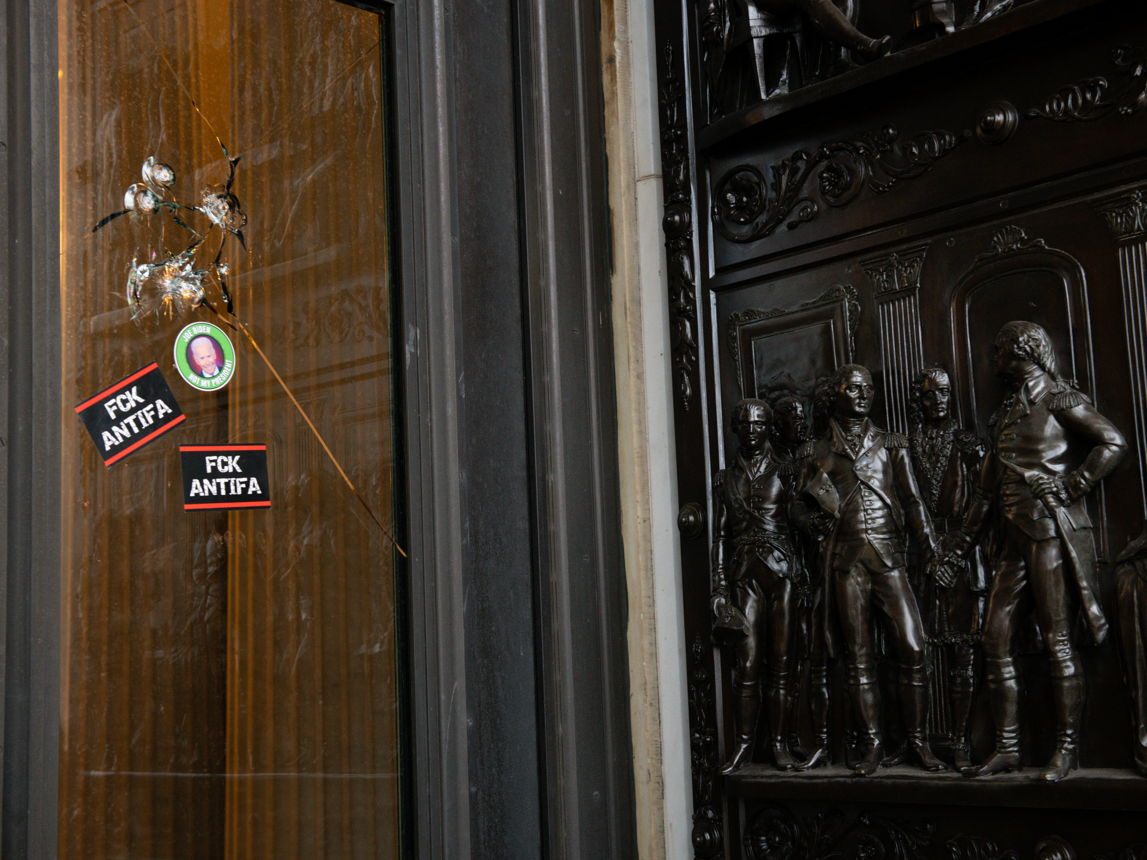 caption: Stickers reading "Fck Antifa" are stuck on a broken window at the U.S. Capitol after the building was breached by rioters on Jan. 6.