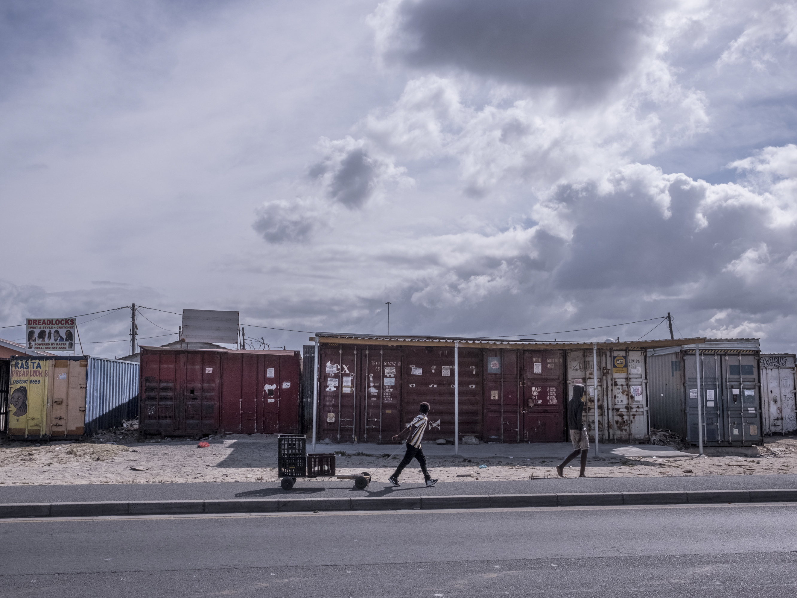 caption: Boys walk past shuttered businesses in the township of Khayelitsha in Cape Town, South Africa, during the coronavirus lockdown. This recession is the first triggered solely by a pandemic, and low-income countries are particularly hard-hit.