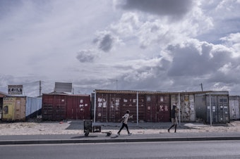 caption: Boys walk past shuttered businesses in the township of Khayelitsha in Cape Town, South Africa, during the coronavirus lockdown. This recession is the first triggered solely by a pandemic, and low-income countries are particularly hard-hit.