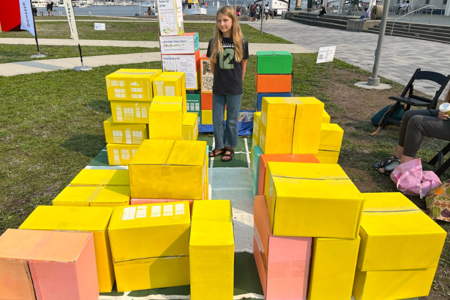 caption: Seattle middle schooler Mila Fedorchenko takes part in a design festival during the summer of 2023. Students were asked to design functional cities. They were given a set amount of boxes, which represented the amount of growth they had to make room for, considering homes and services. Mila found that she needed to stack some buildings on top of each other in order to make enough room for parks.