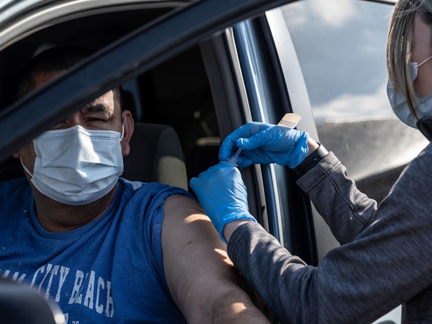 caption: A medical professional from UofL Health administers a vaccine to a patient in their vehicle at University of Louisville Cardinal Stadium.