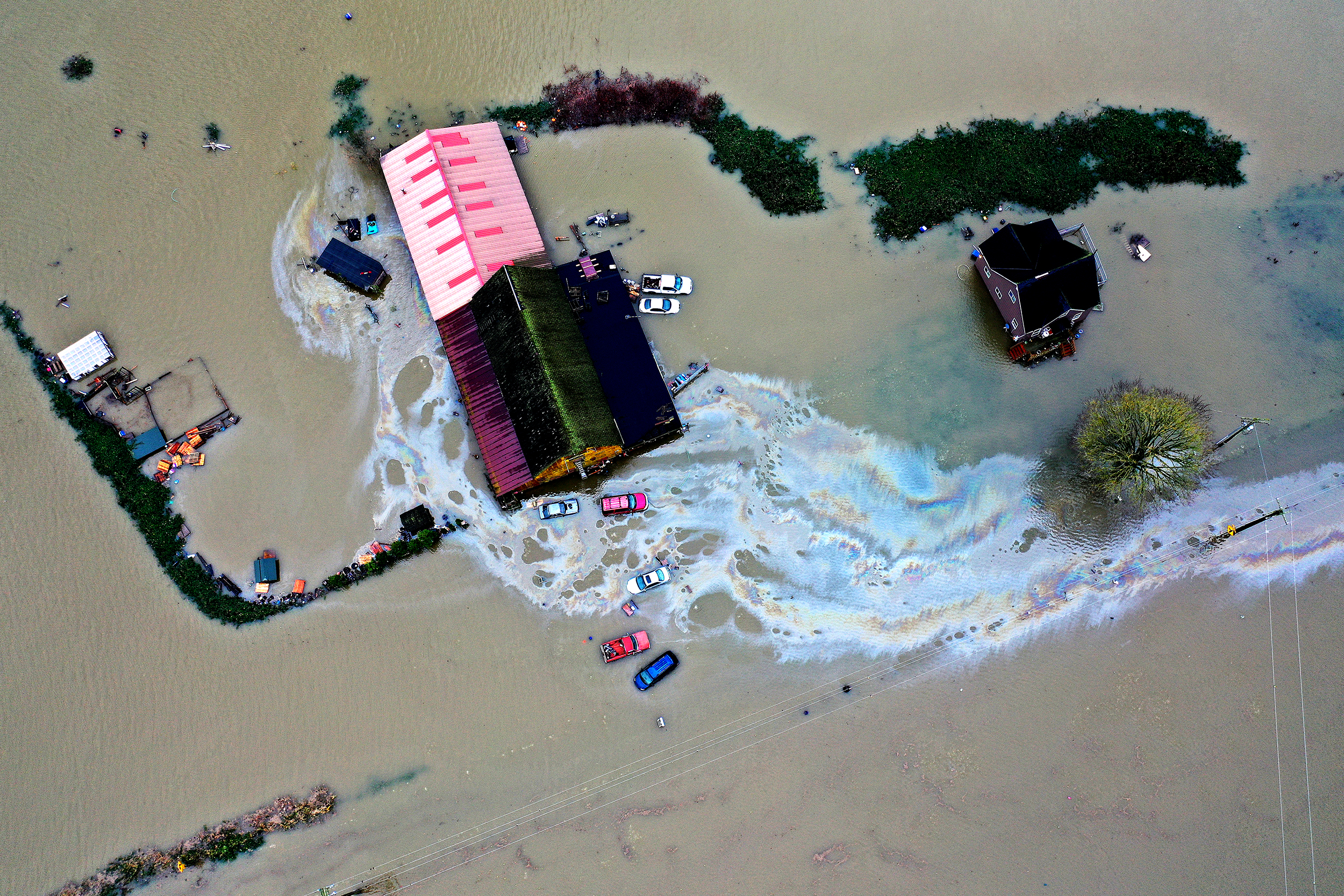 caption: Homes are shown surrounded by floodwater and what appears to be gasoline following consecutive atmospheric rivers on Thursday, December 11, 2025, near Mount Vernon. 