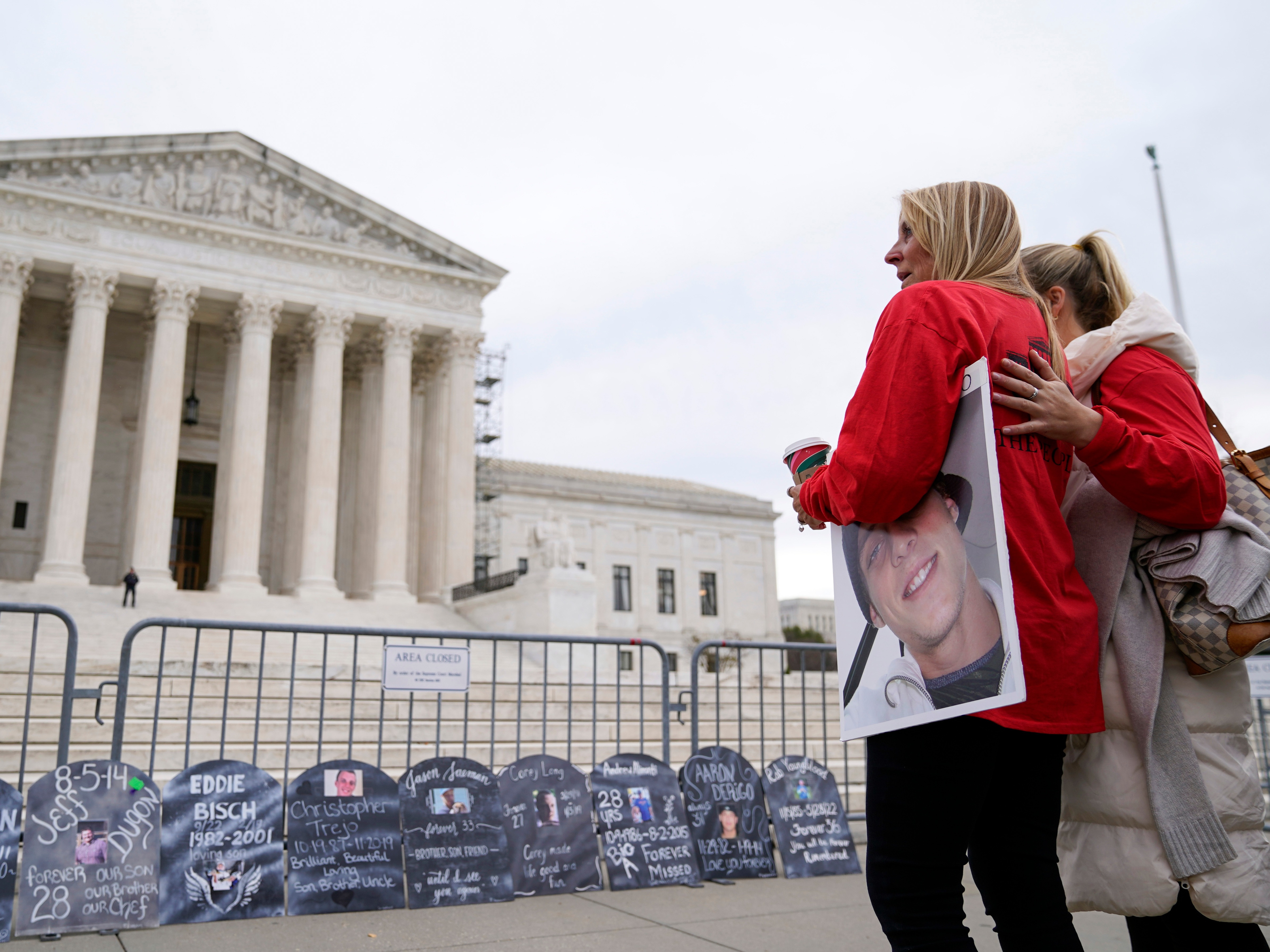caption: Jen Trejo holds a photo of her son Christopher as she is comforted outside the Supreme Court on Dec. 4, 2023, in Washington.